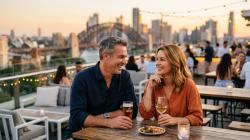 Confident Australian couple in their late 40s sharing a relaxed evening at a stylish Sydney rooftop bar at golden hour
