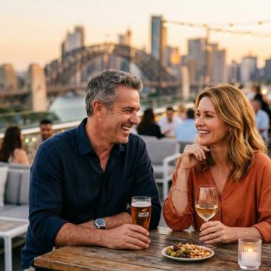 Confident Australian couple in their late 40s sharing a relaxed evening at a stylish Sydney rooftop bar at golden hour